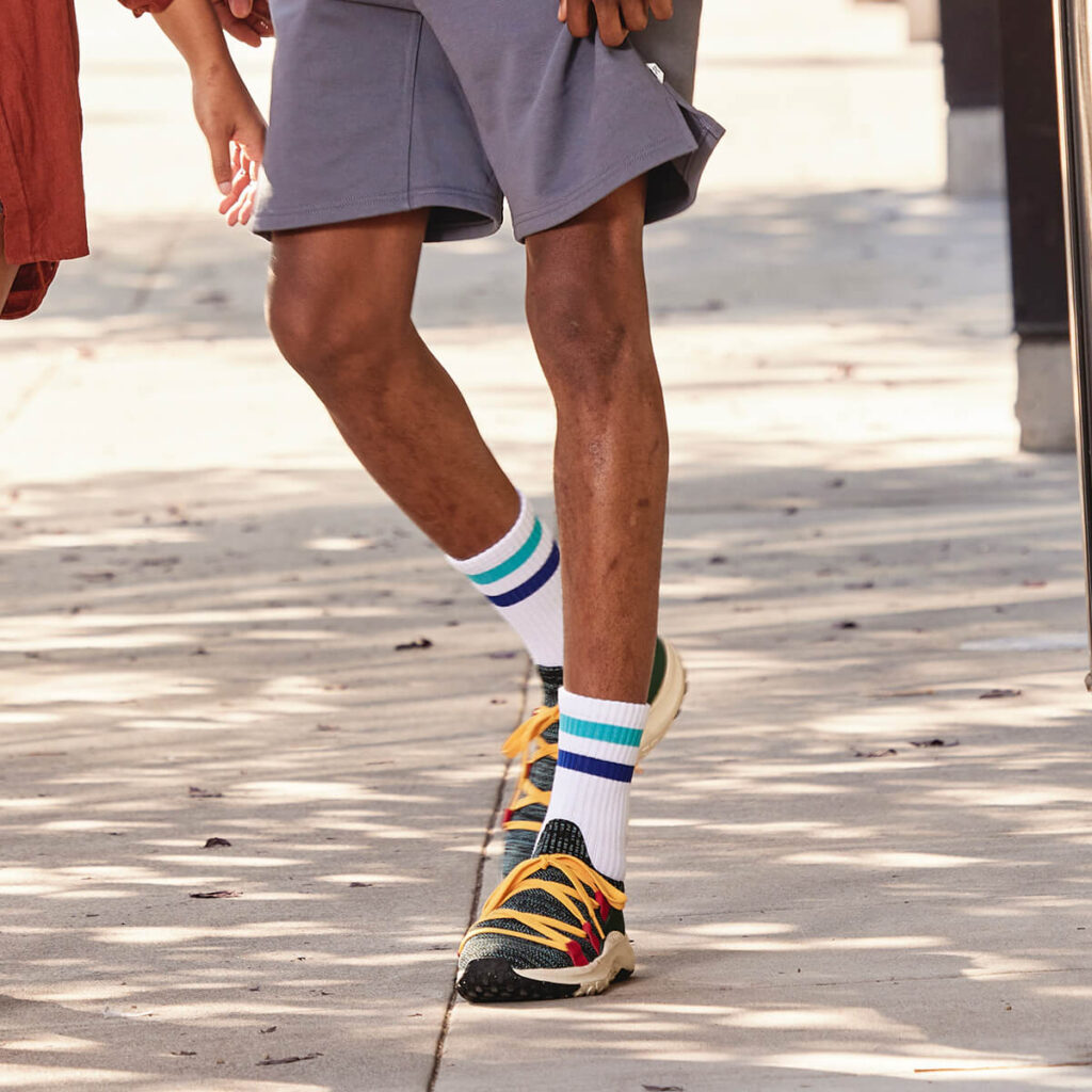 black man walking on the side walk in gray short and green shoes