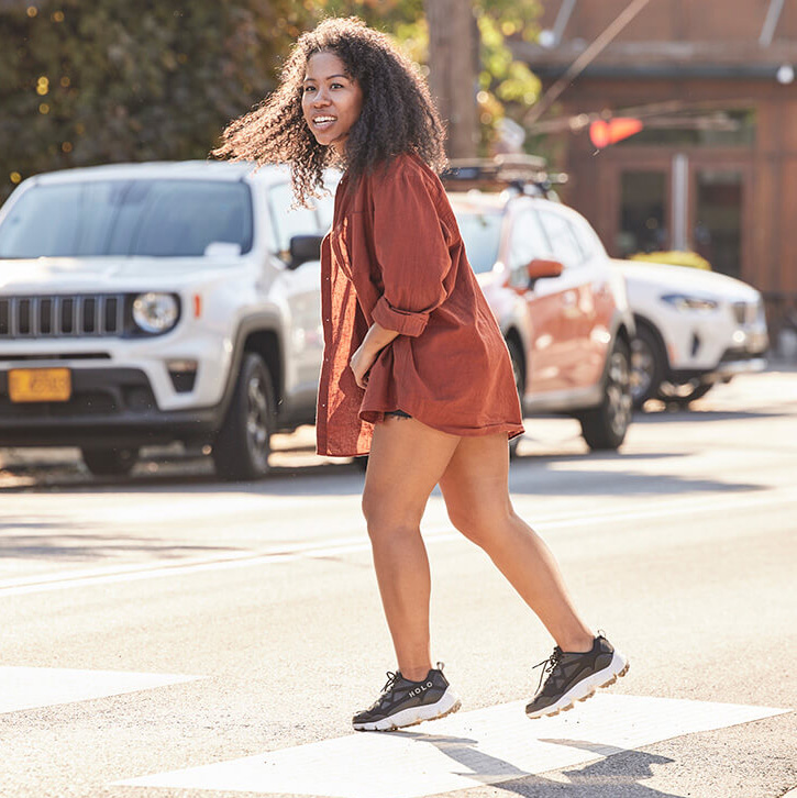 black woman crossing the street in a rust orange shirt and black shoes
