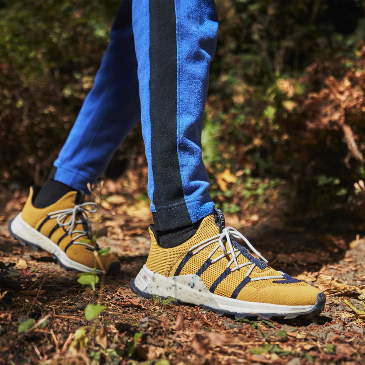 man walking on trail in blue sweatpants and yellow sneakers