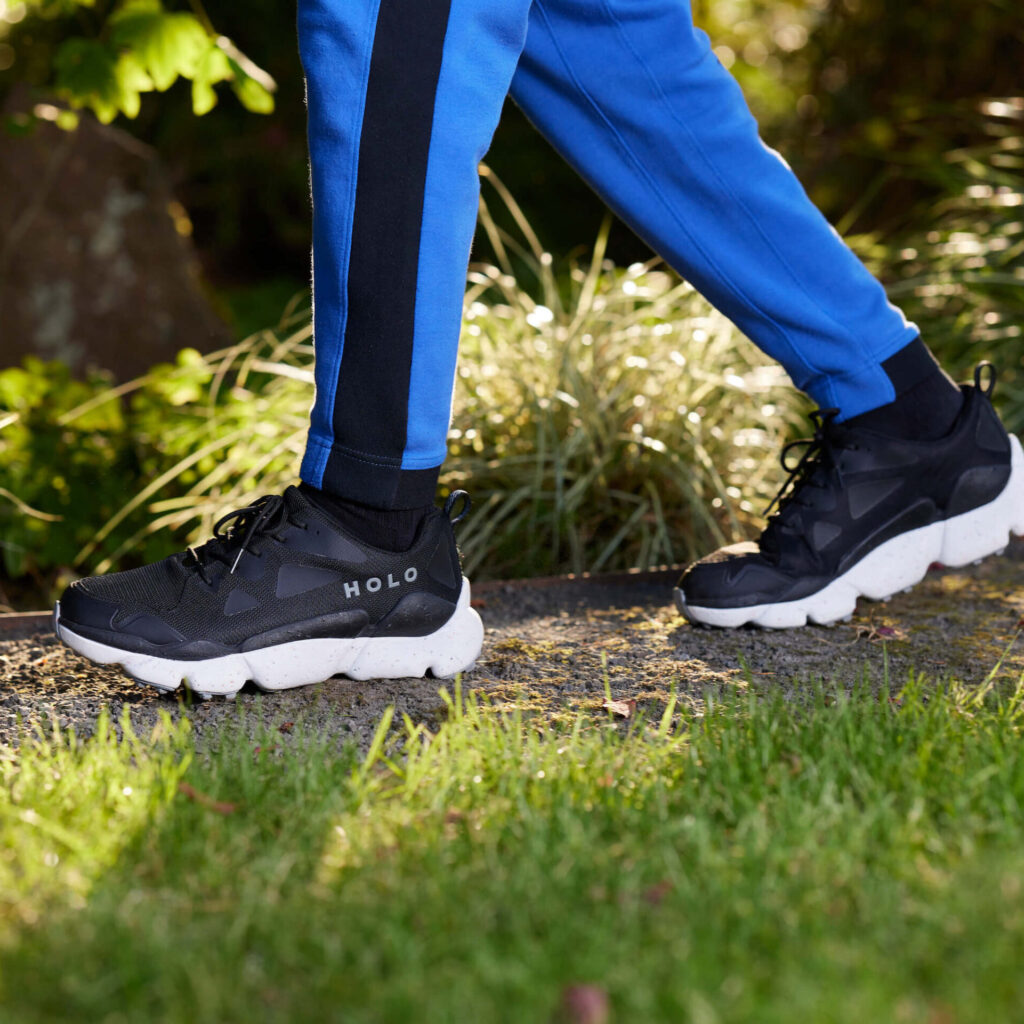 person walking on a paved path next to grass in blue sweatpants and black shoes