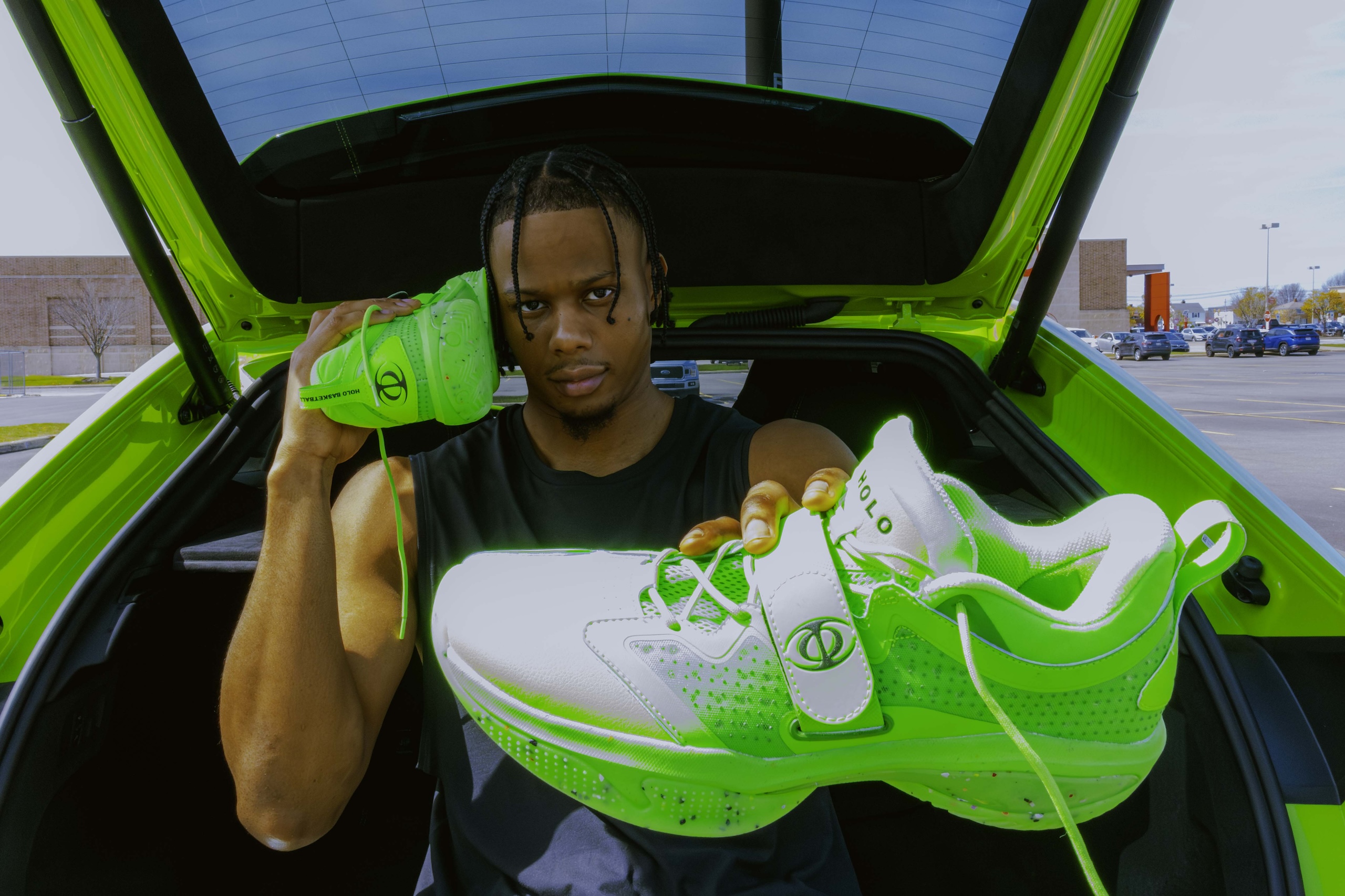 isaac okoro holding green pairs of holo shoes outside